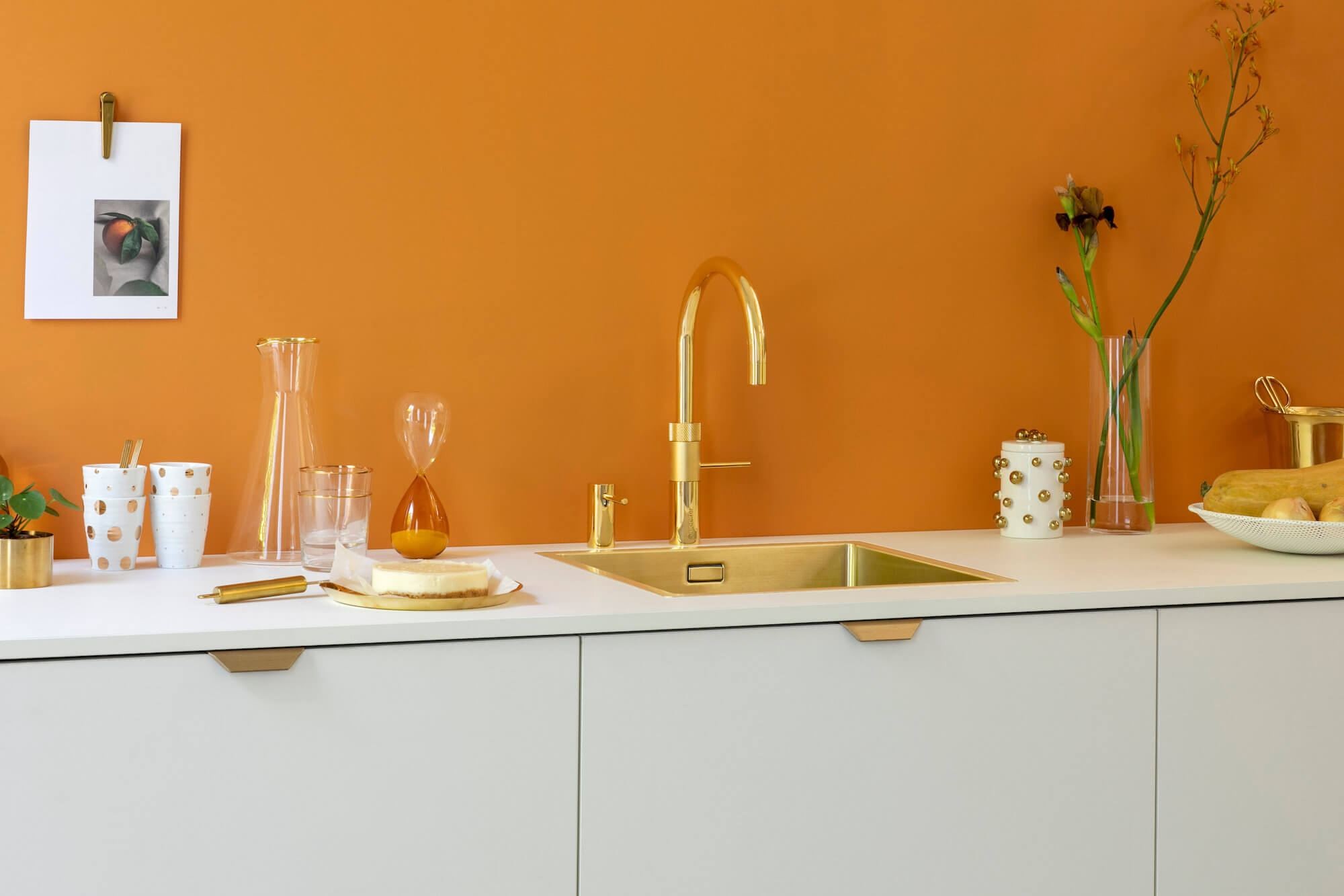 Quooker Wasserhahn in Gold vor einer orangen Wand